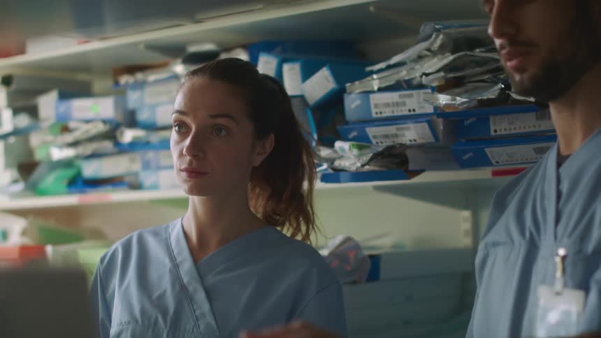 Two healthcare workers are having a discussion in a room filled with supply shelves