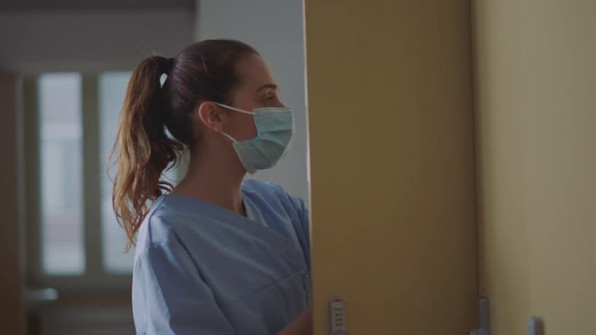 Masked female nurse opening her locker at work
