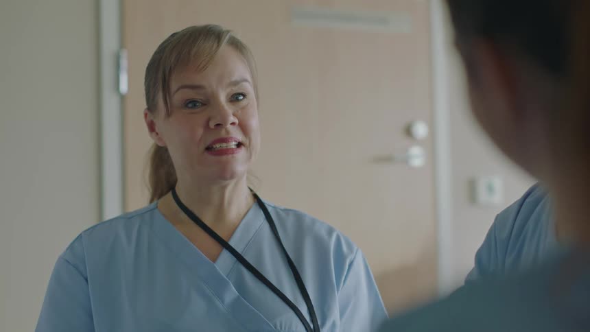 A nurse in a hallway talks with a man in scrubs when another nurse walks over and joins them