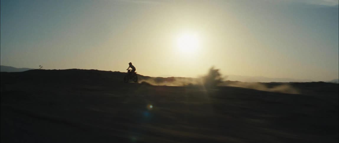 A motorcyclist rides an offroad motorcycle through a desert during the day