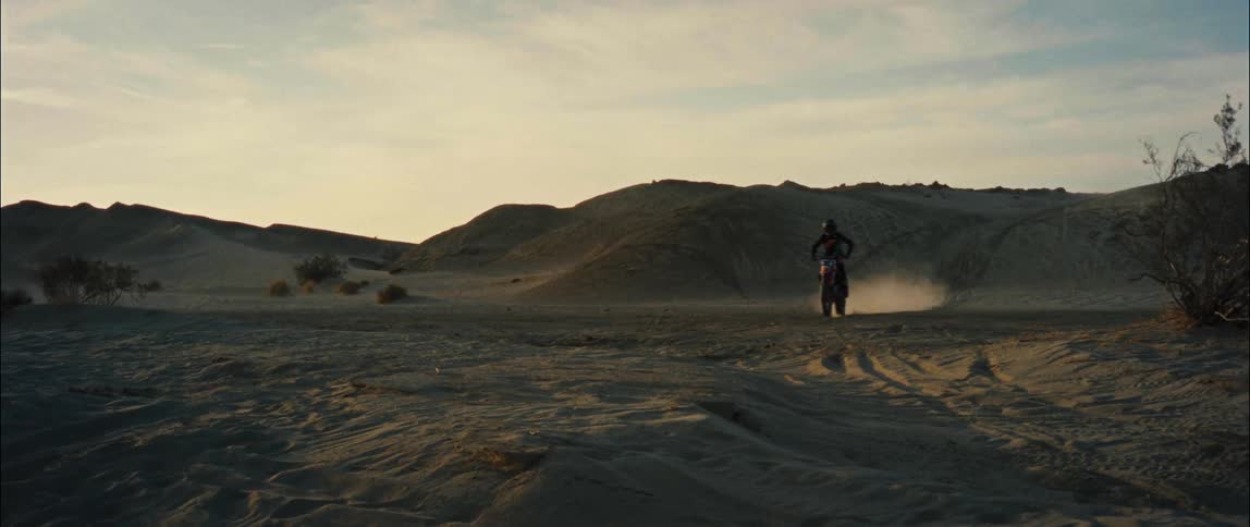 A person drives a motorcycle across a sandy landscape