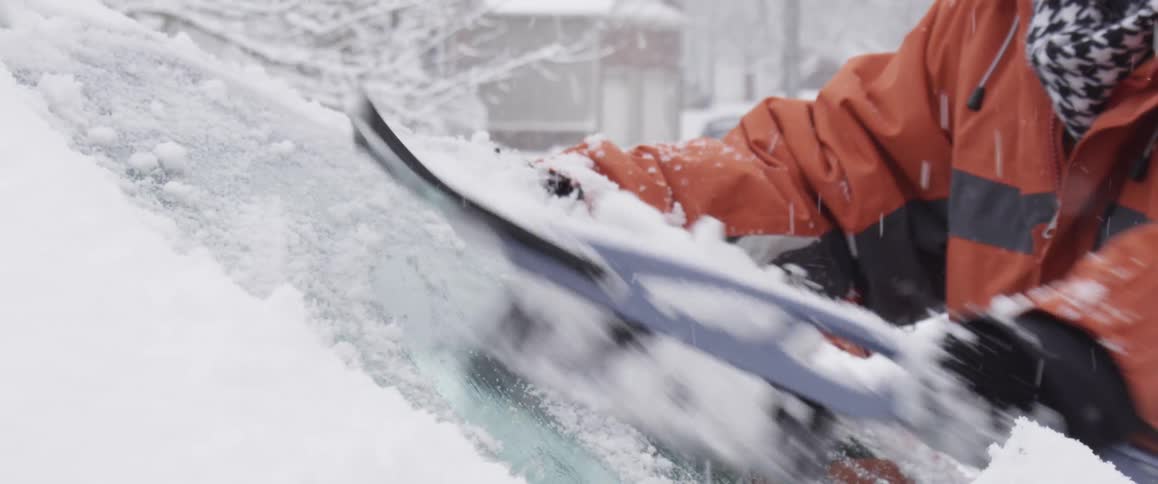 A woman brushing snow off a windshield on a snowy day