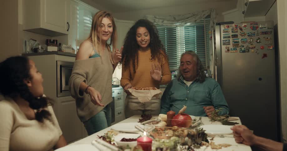 A woman sets a dish of food down a table as friends cheer