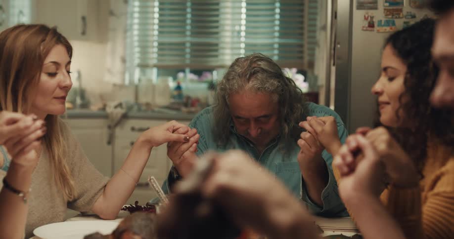 Friends hold hands while saying grace at the dinner table