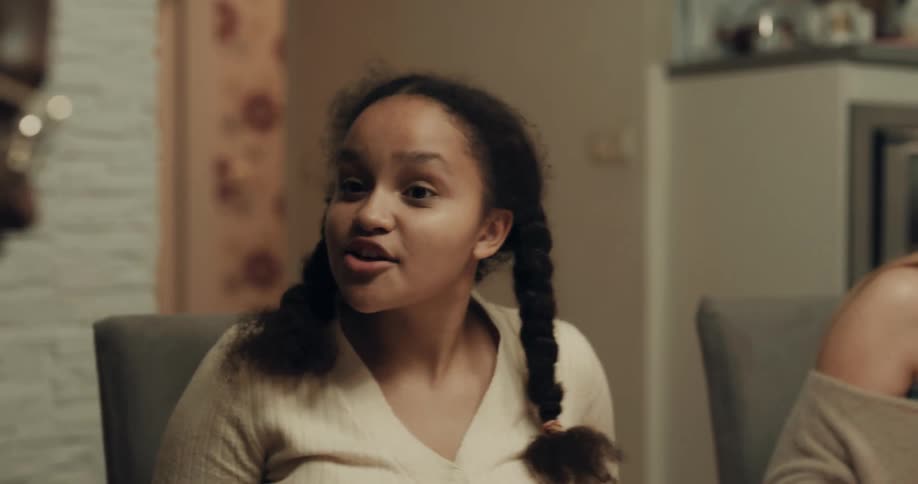 A teenaged girl talks and laughs while eating dinner with a group of people in a home kitchen