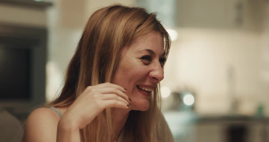 A woman throws her hand up while laughing during a conversation in her kitchen