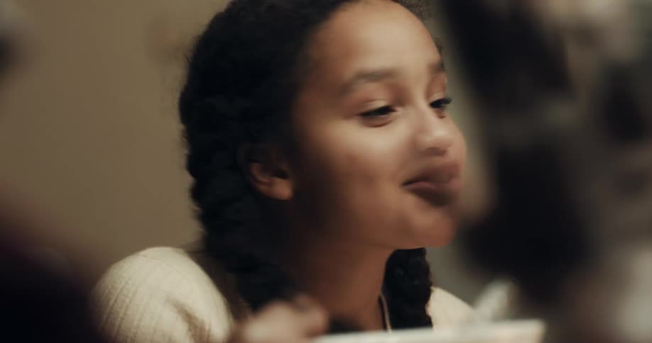 A young woman laughs as she helps pass food along to friends at dinner