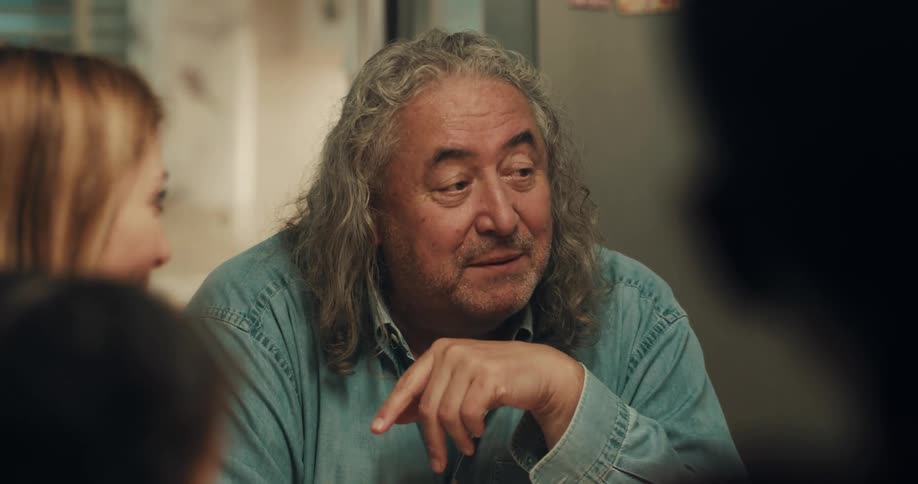 A man gestures with his hands as he speaks to a group of people gathered around a table