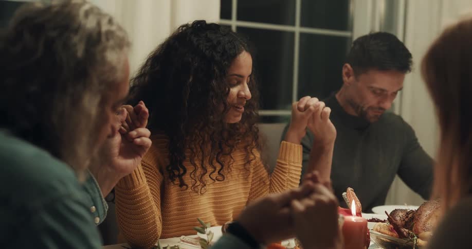 Friends holding hands saying grace at thanksgiving dinner