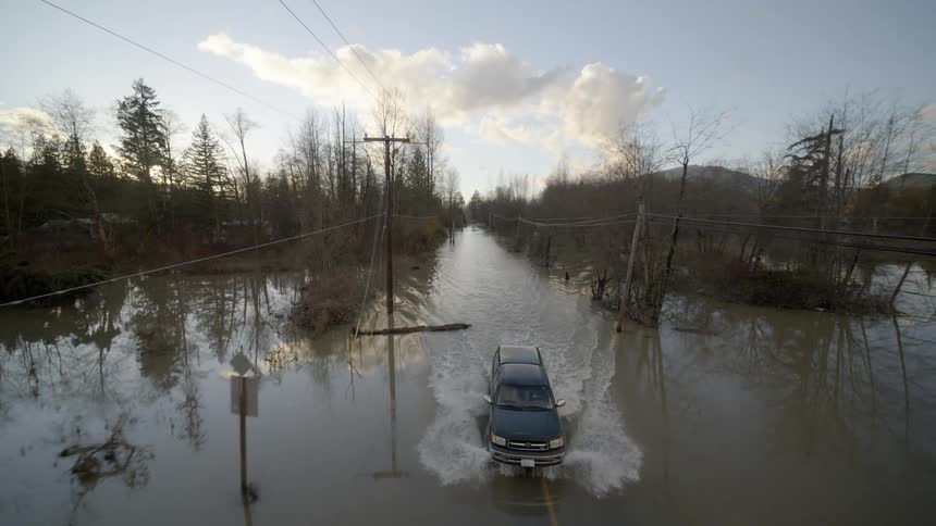 A pickup truck leaves a wake as it drives around debris traveling along a partially flooded roadway