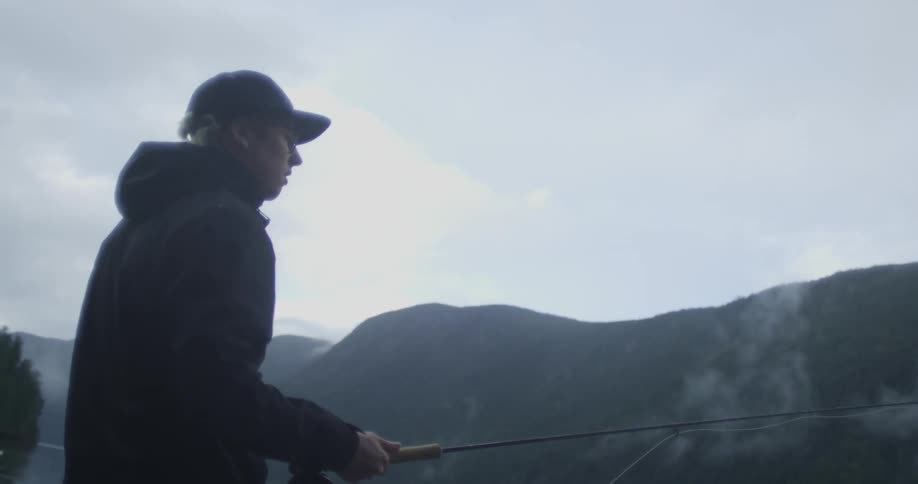 A man is standing near a lake and fishing