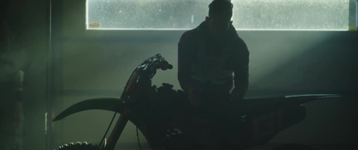 A man puts a part back on his motorcycle while working in his garage