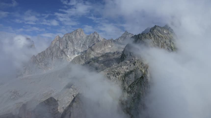 The rocky peak of a mountain ridge shrouded in clouds during the day