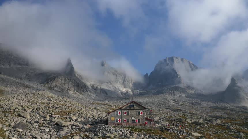 People walk around the rifugio gianetti mountain hut on a bright blue sky day