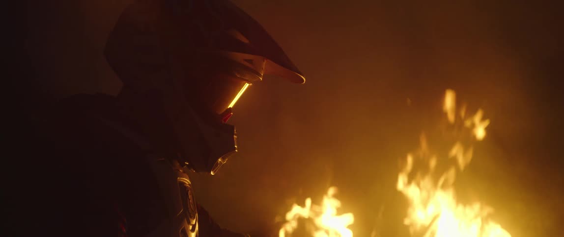 A person wearing a helmet and goggles is looking at the flames of a bonfire