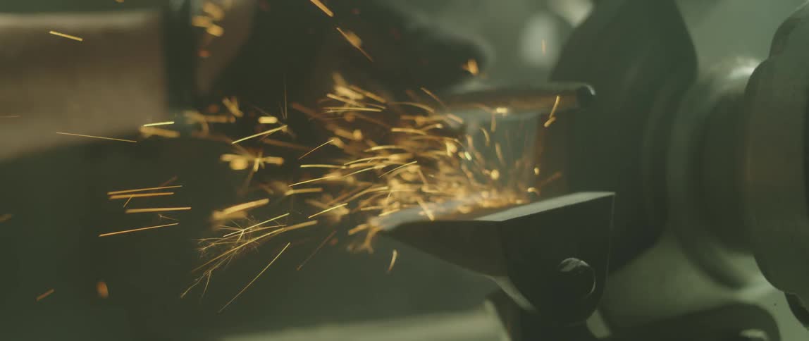 Sparks fly as a person shapes a metal rod with a power tool