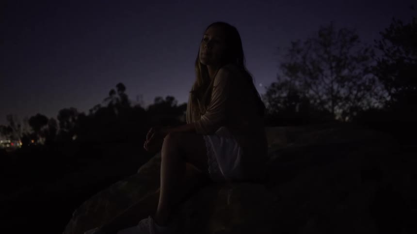 A woman leans forward while watching a view from a hill at night