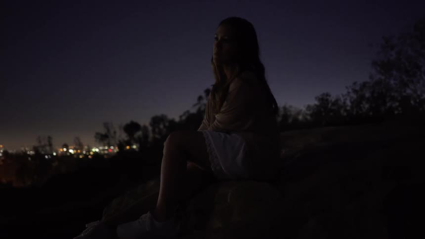 A woman sits in the dark overlooking a city at night