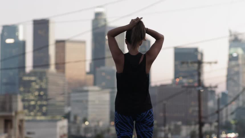A woman wearing jogging clothes stands in the middle of a street and pulls her hair back