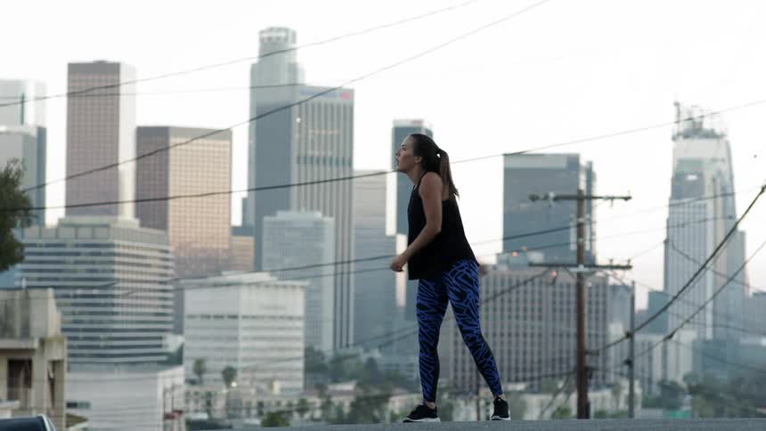 A woman is jumping around stretching in the street