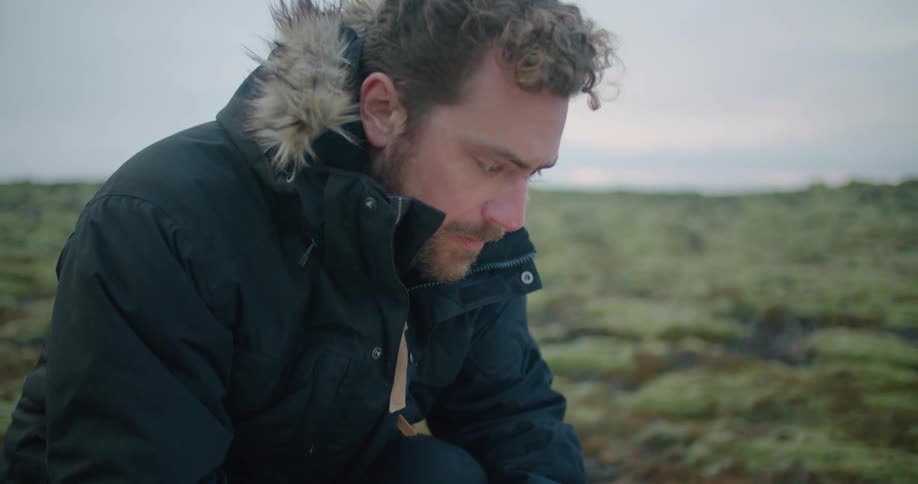 A man types on his laptop while kneeling in a field