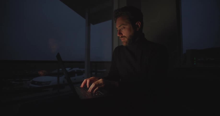 A man is typing on his laptop in the dark room