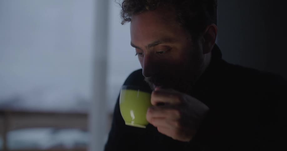 A man is using his cell phone and drinking coffee