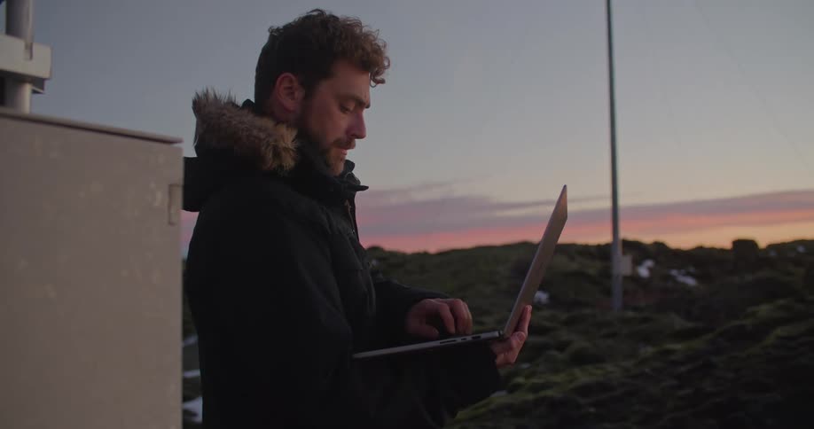 A man observes a windmill and types notes into his laptop
