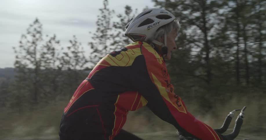 Older cyclist rides past two people sitting on bench in a scenic area