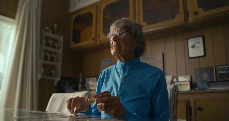 Grandmother plays solitaire over the dinning table at home while watching television