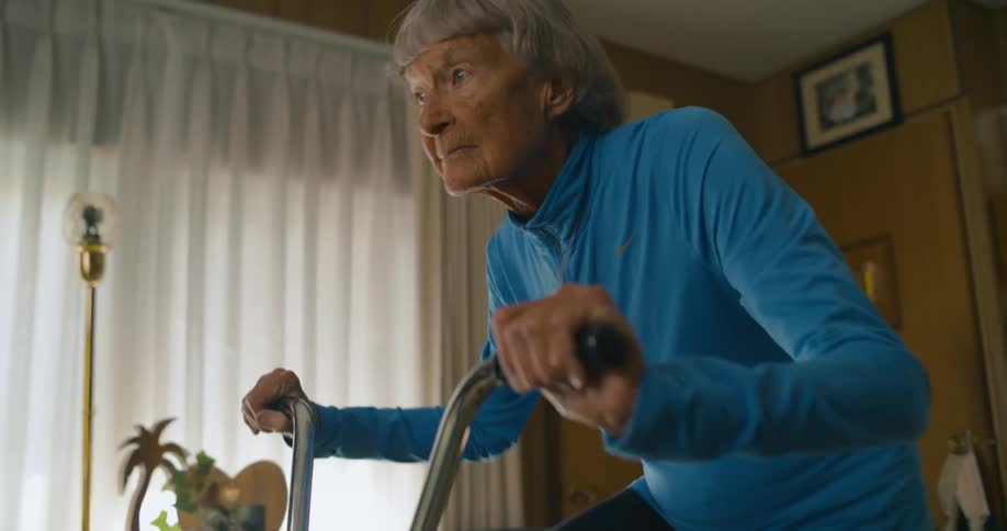 An elderly woman rides a dated exercise bike indoors