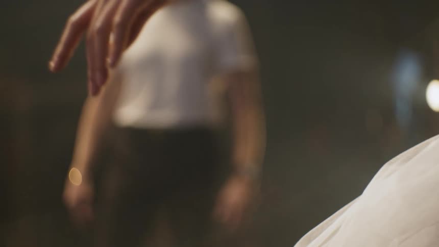 A man walks on stage and watches as a ballerina in a tutu raises her arm in dance