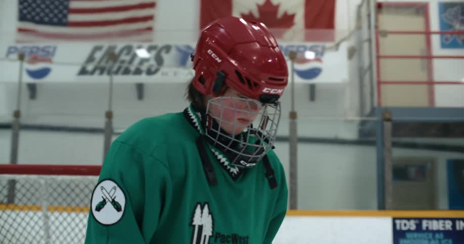 Teenage hockey player drops hockey stick and shakes gloves loose before taking off helmet