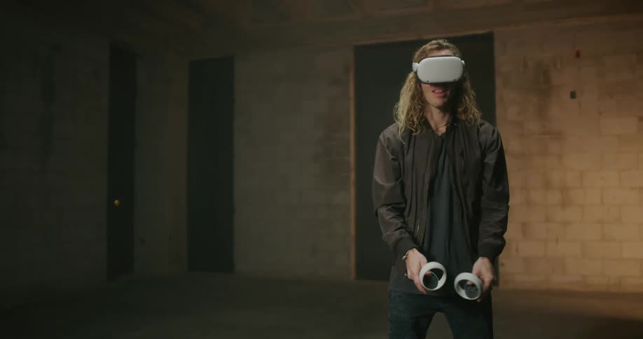 Young blonde long haired man playing videogames with 3d virtual reality goggles over his eyes