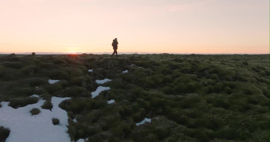Silhouette of a person walking across the top of mountain ridge as the sun is setting on the horizon