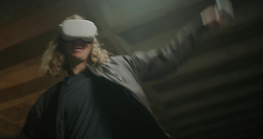 Blonde man plays game while wearing vr headset in room with exposed rafters