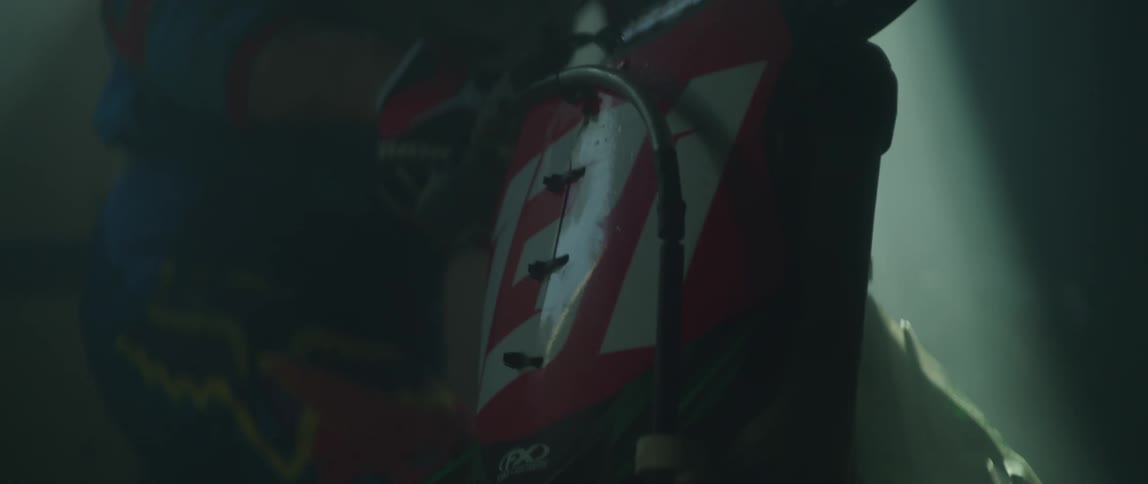 A man removes his hand from his dirt bike and steps on the kickstand and walks away