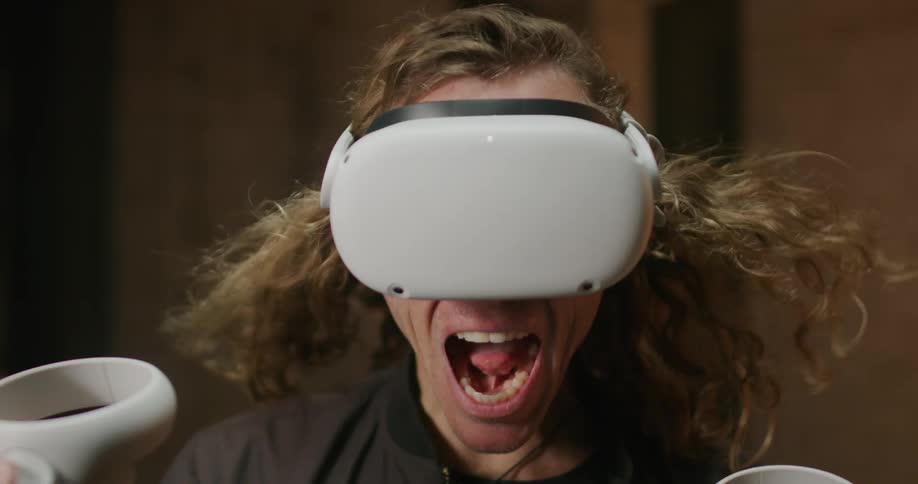 A man shouts while playing a virtual reality game as his hair waves in the wind and lights flicker above him