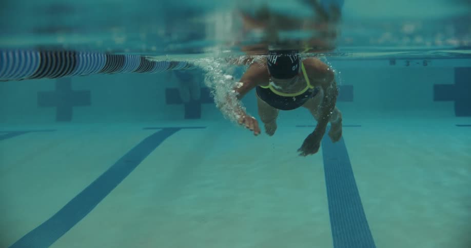 An elderly woman swims down a lane of an olympic size swimming pool