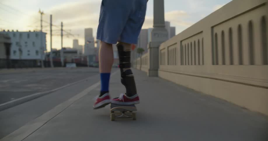A pedestrian is skateboarding on a sidewalk in an urban city