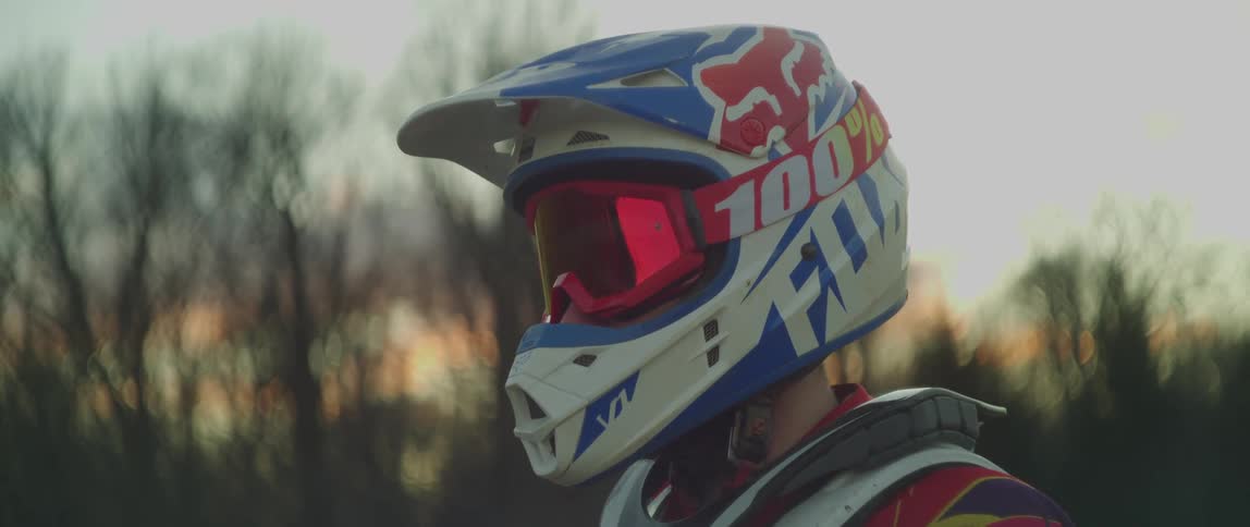 Person wears motorcycle crash helmet outdoors with leafless trees in background