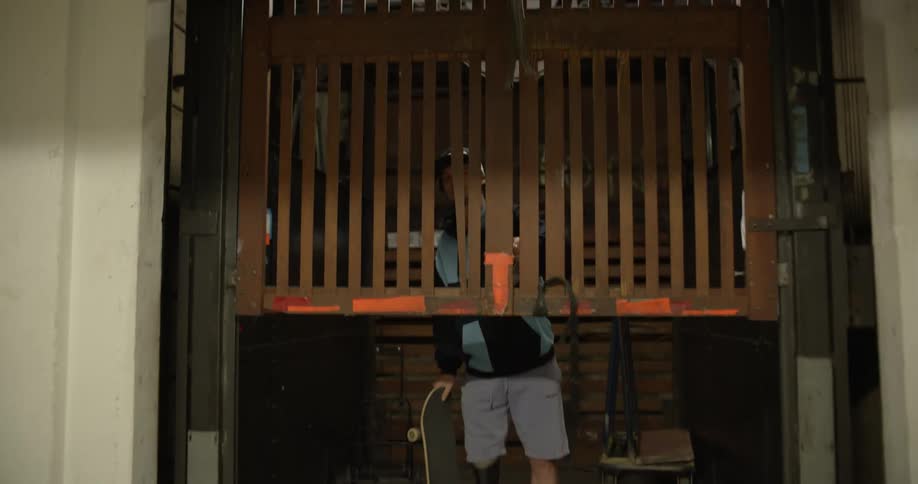 Skateboarder with prosthetic limb pushes up elevator gate before exiting carrying a skateboard