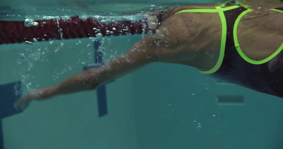 Elderly woman swims along swim lane wearing goggles and a cap