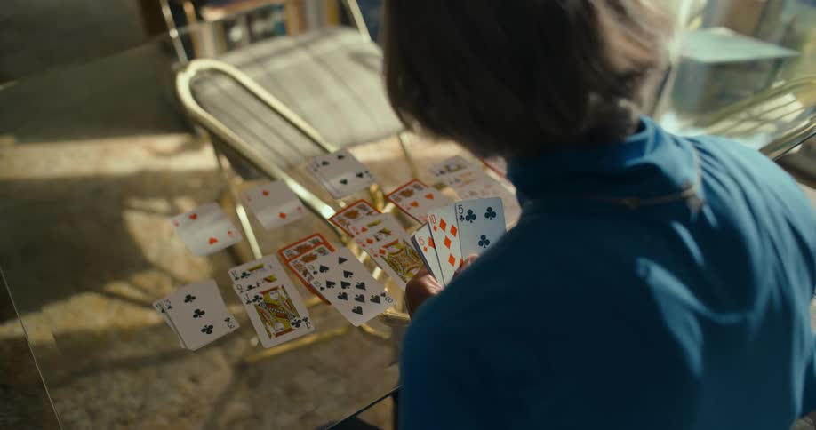 Elderly woman playing solitaire on a glass table indoors