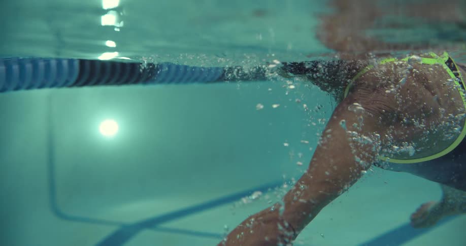 Old woman wearing black swimsuit and swim cap swimming on an olympic pool