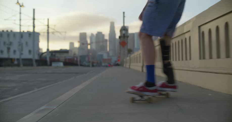 Skateboarder with prosthetic leg rides along highway toward city skyline