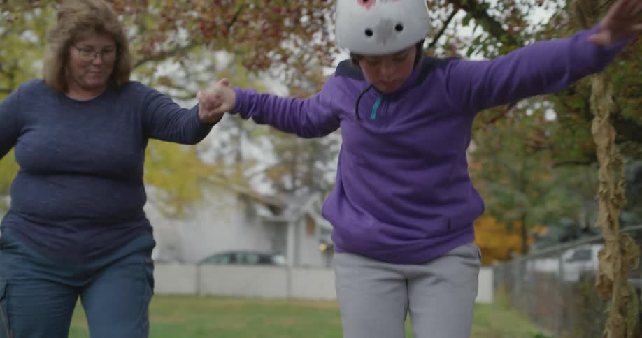 A young person calls over a woman to help balance them on roller blades outside