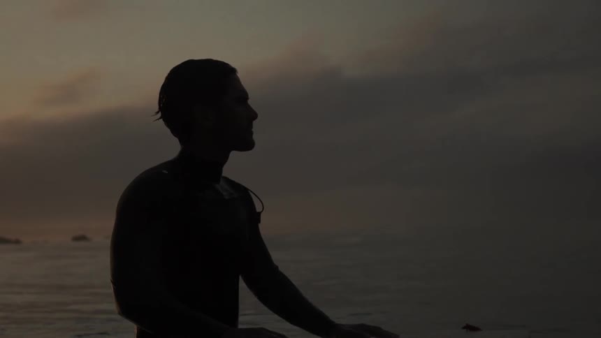 A man looking around while standing in the ocean at sunset