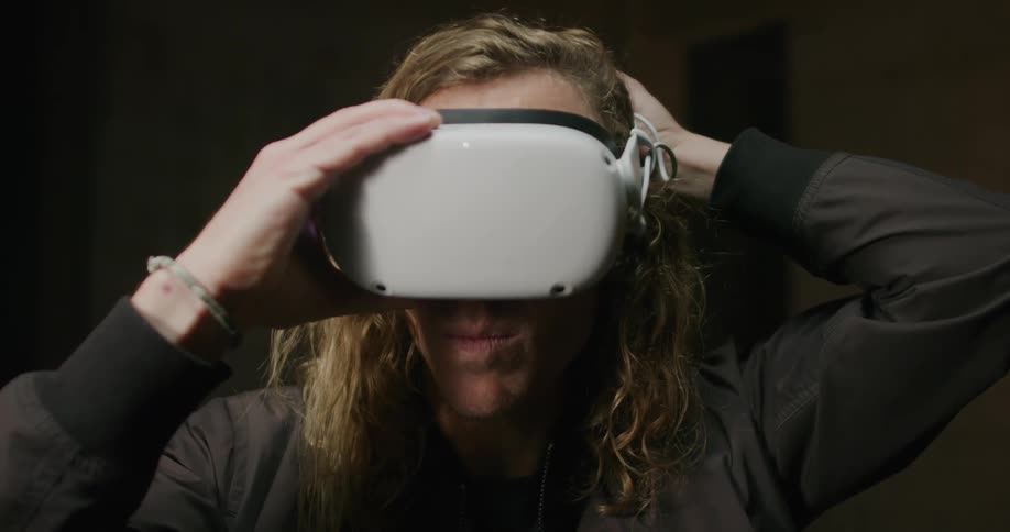 A man with long blond hair puts on a virtual reality headset