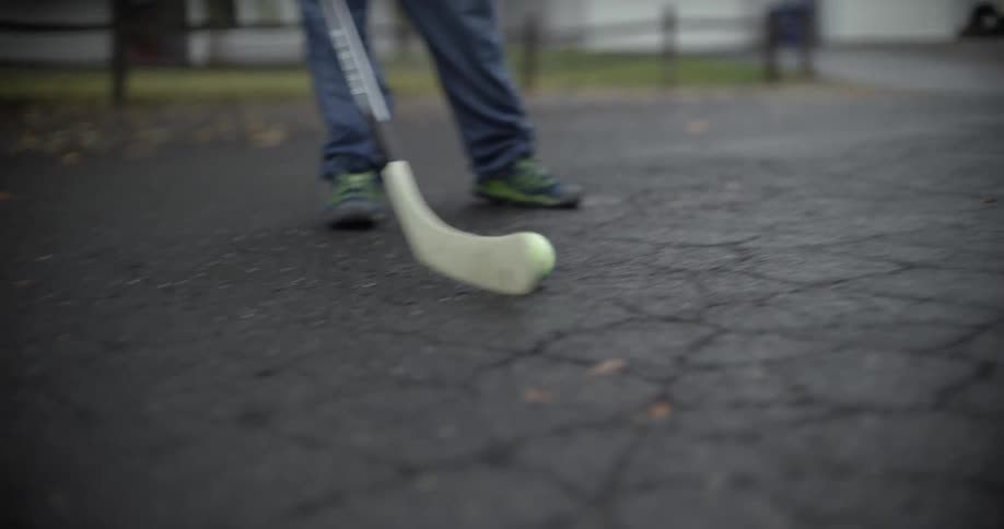 A girl is using a hockey stick to move a ball around on a street